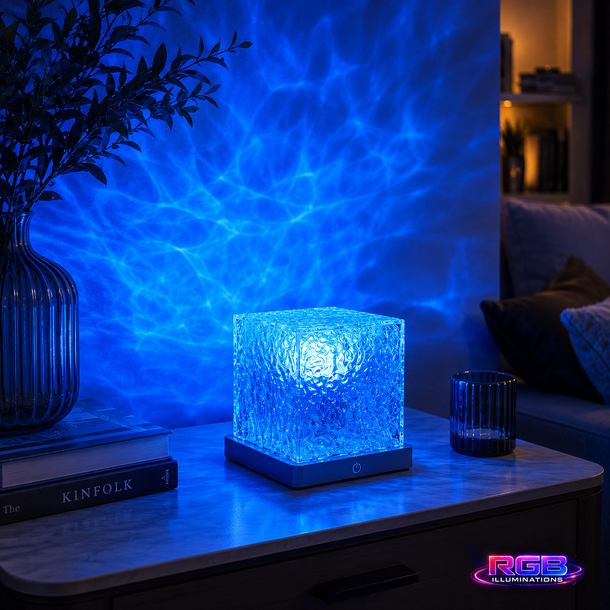 A square LED wall light projector casting a rippling water pattern on a wall, shown on a wooden table next to a glass vase and a small cup. — RGB Illuminations product view 6