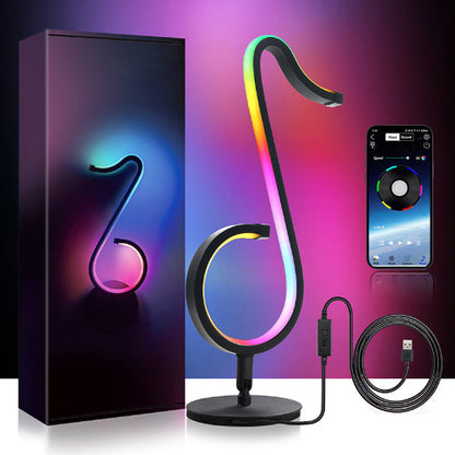 Colorful lamp shaped like a musical note with packaging, smartphone, and cable on a reflective surface.