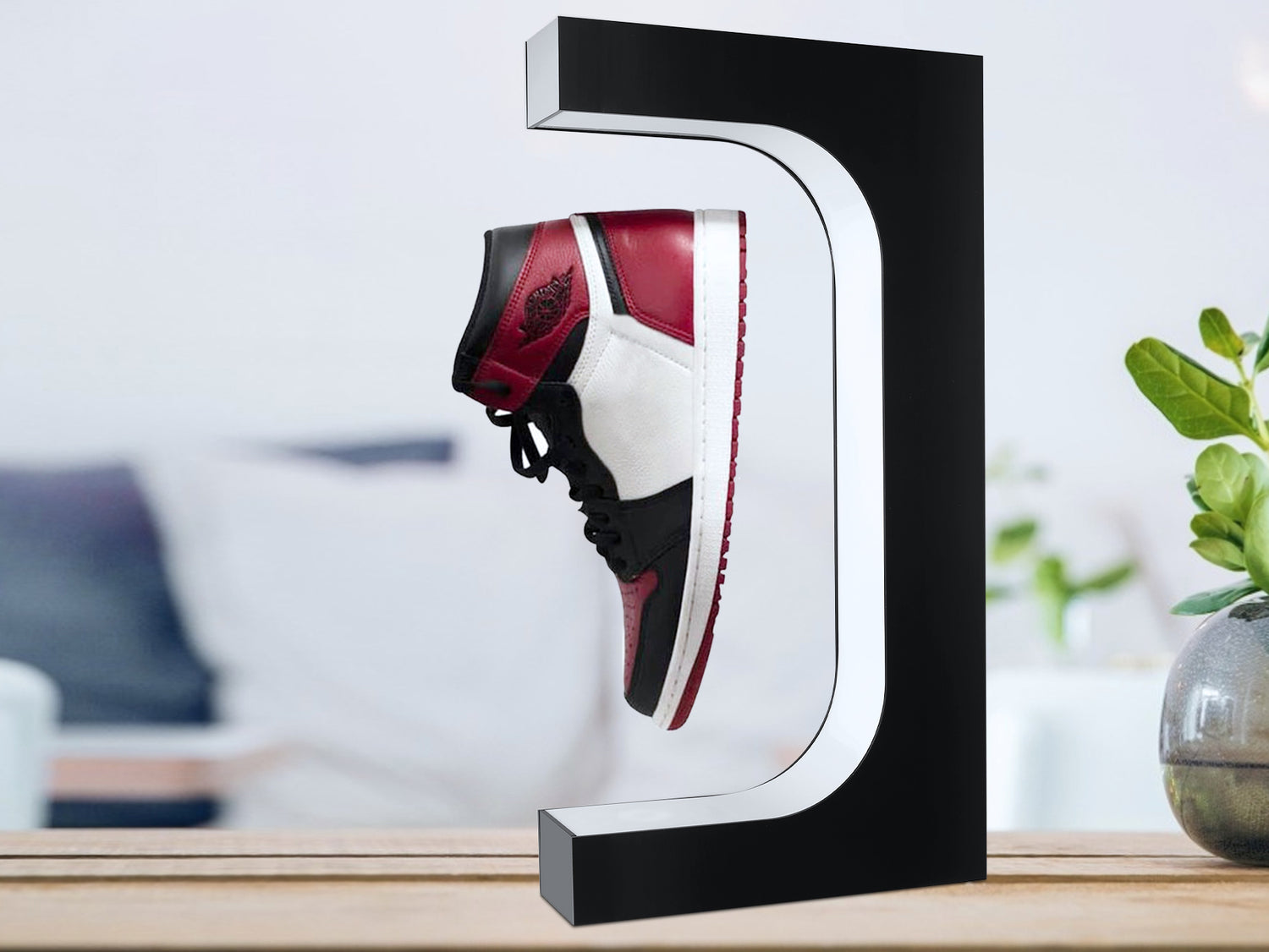 Sneaker displayed on a black and white stand in a room with a laptop and plant.